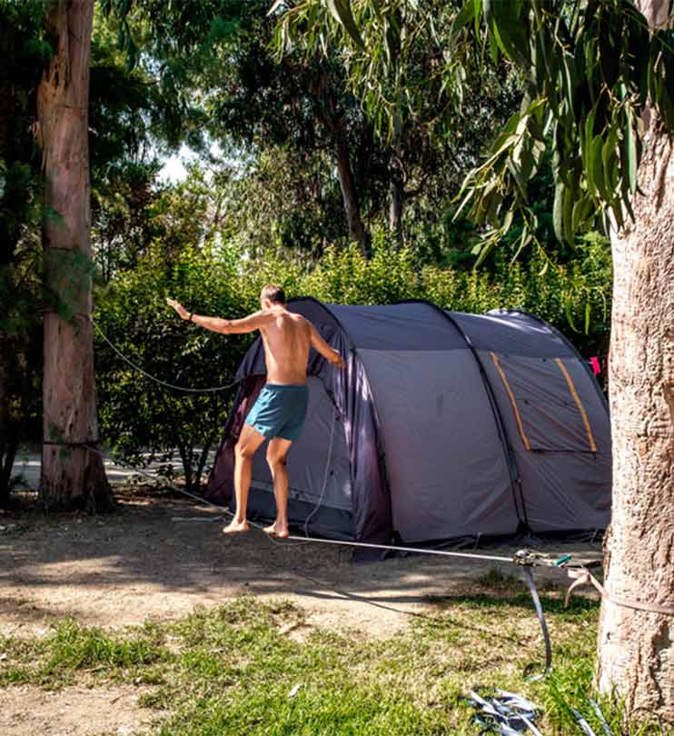 Homme s'exerçant à la slackline devant sa tente sur son emplacement nu